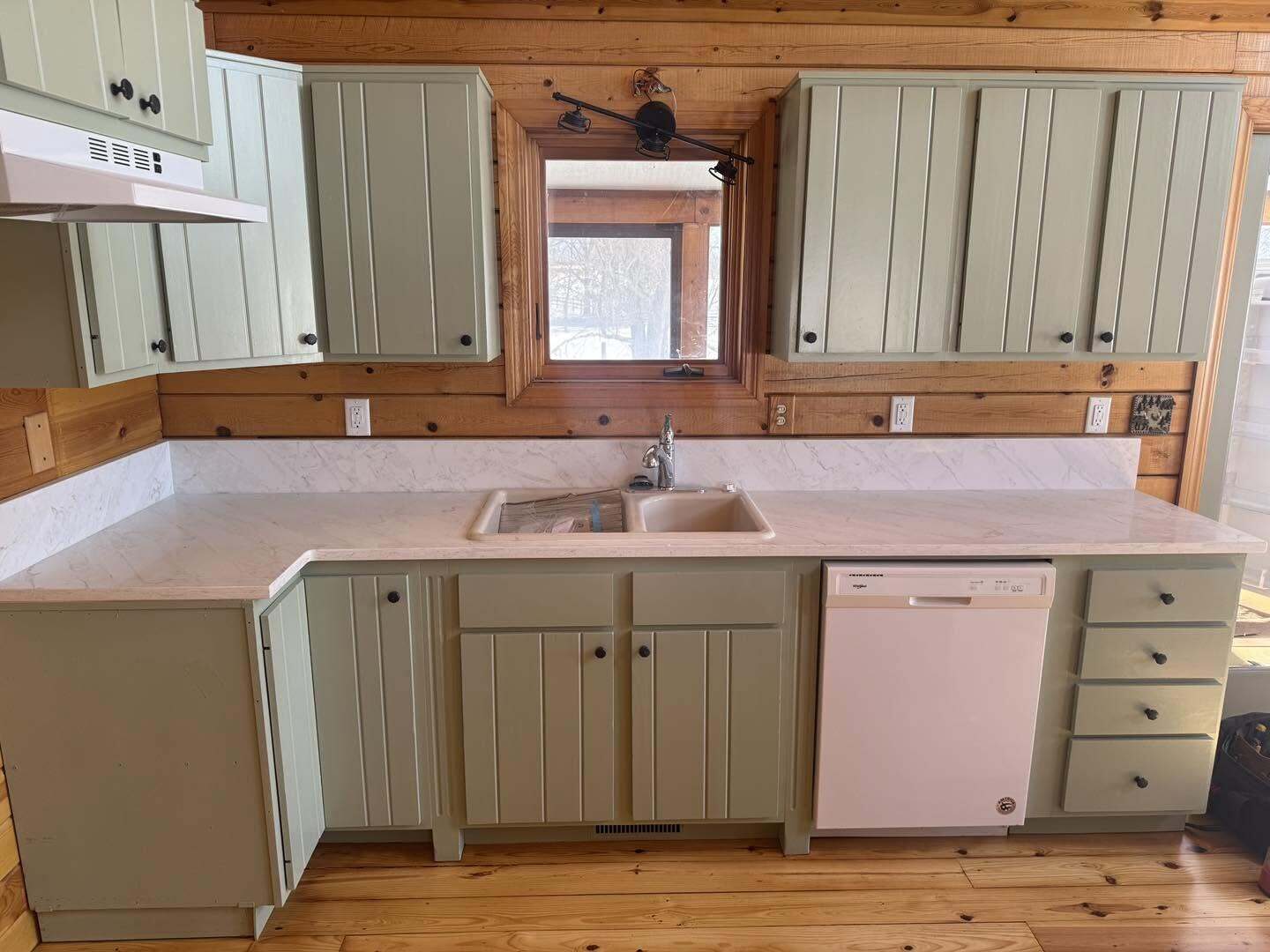 Kitchen with sage green cabinets, light veined countertop, white dishwasher, beige sink and wood plank floor